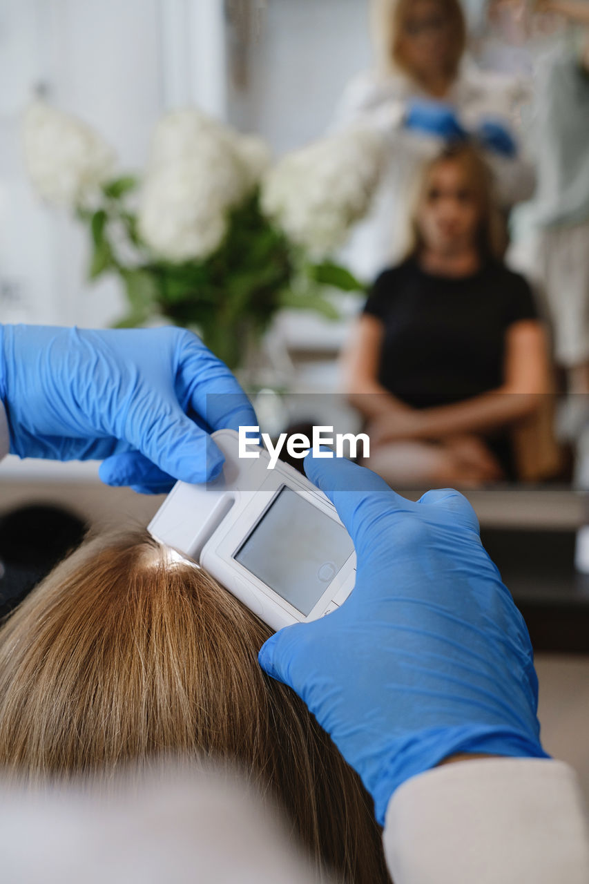 Close up view of female trihologist examines head skin of woman with special dermatology equipment