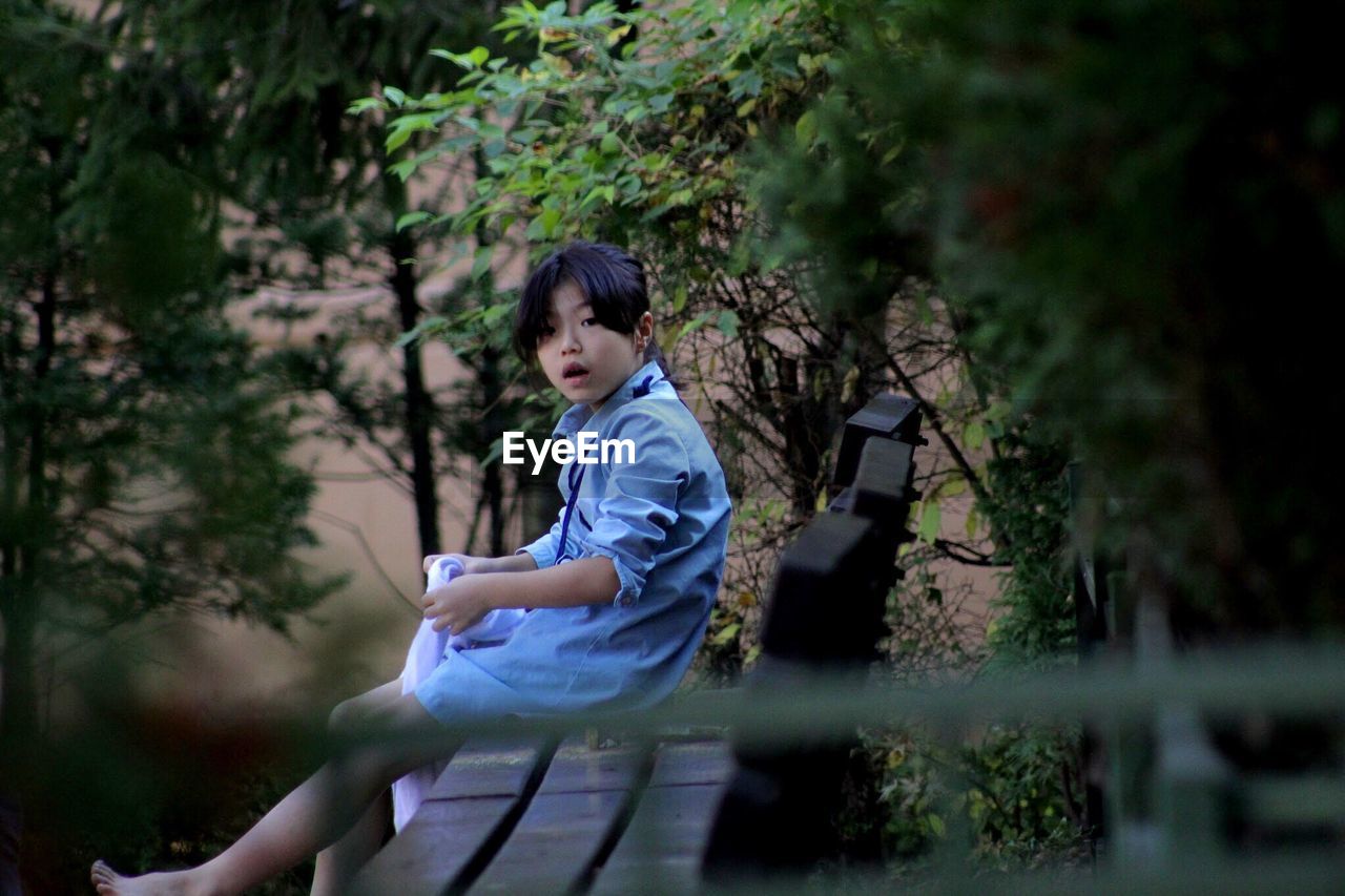 Side view portrait of shocked girl sitting on bench at park