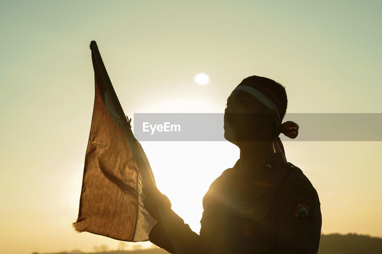 Silhouette man holding flag against clear sky during sunset