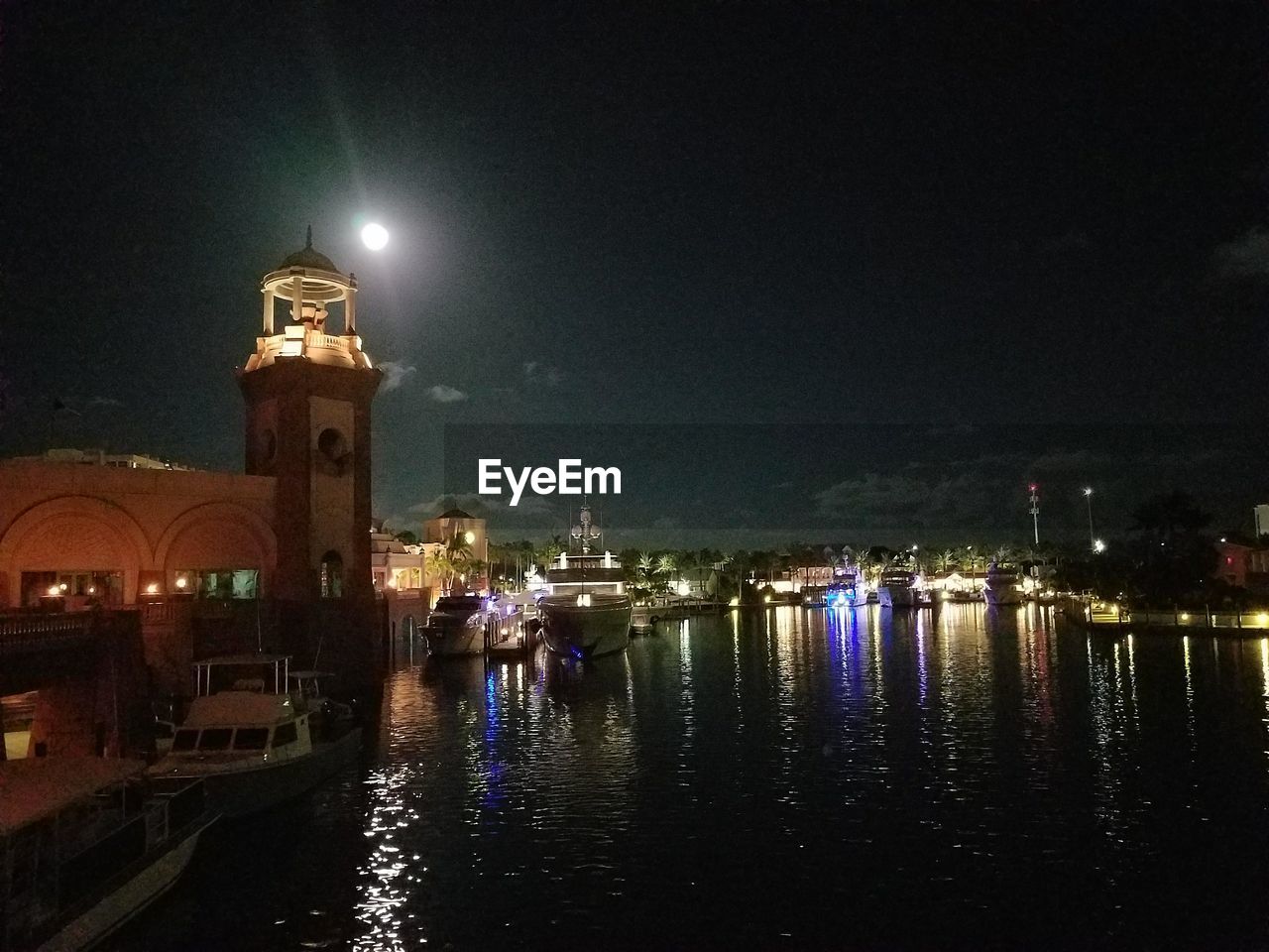 ILLUMINATED CITY BY RIVER AGAINST SKY AT NIGHT