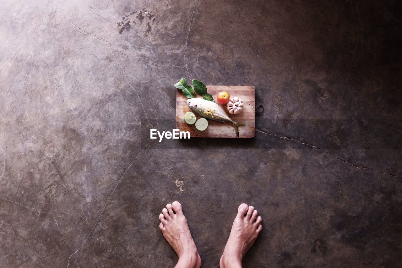 Low section of person standing in front of marinated fish on floor