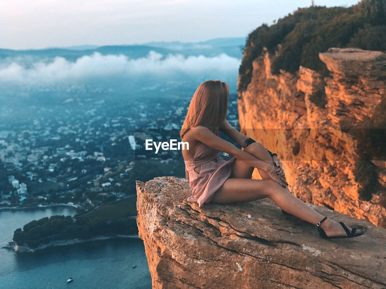 Woman relaxing on cliff against townscape