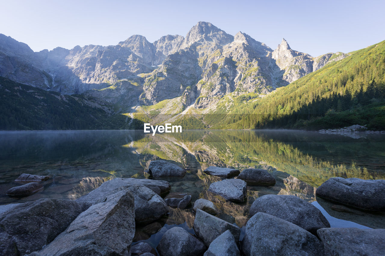 Majestic peak reflecting in pristine crystal clear alpine lake with rocky foreground, poland, europe