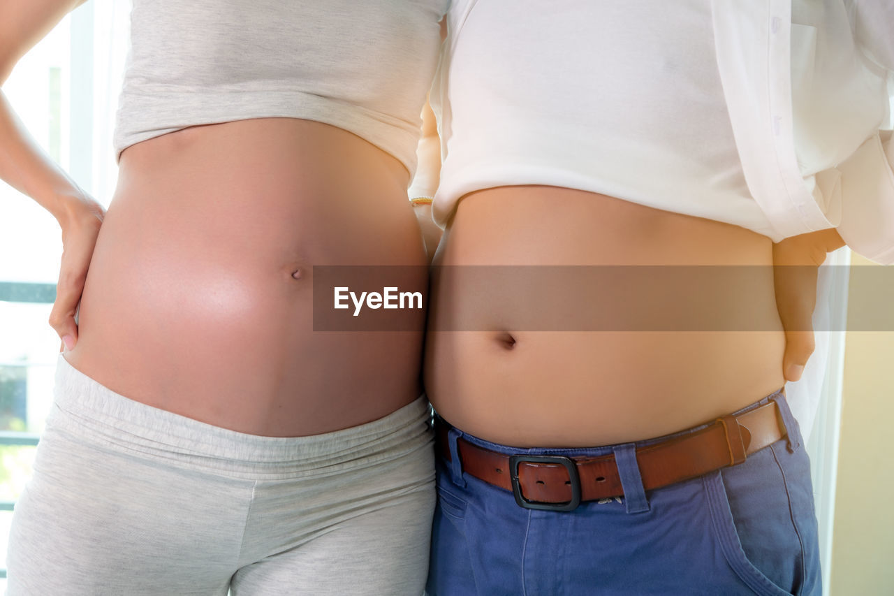 Midsection of pregnant woman with husband standing at home