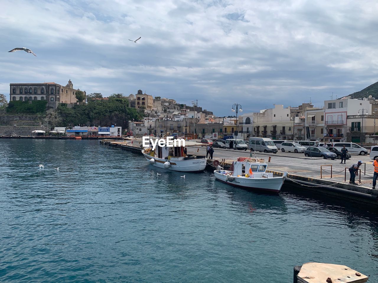 BOATS MOORED AT HARBOR BY CITY AGAINST SKY