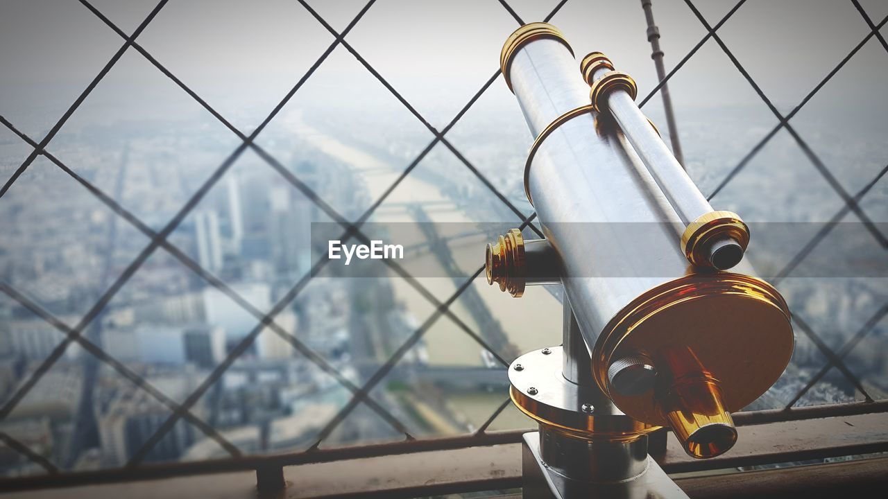 Coin-operated binoculars by chainlink fence in eiffel tower overlooking city