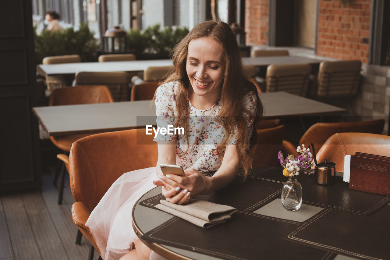 Young woman using phone while sitting on table