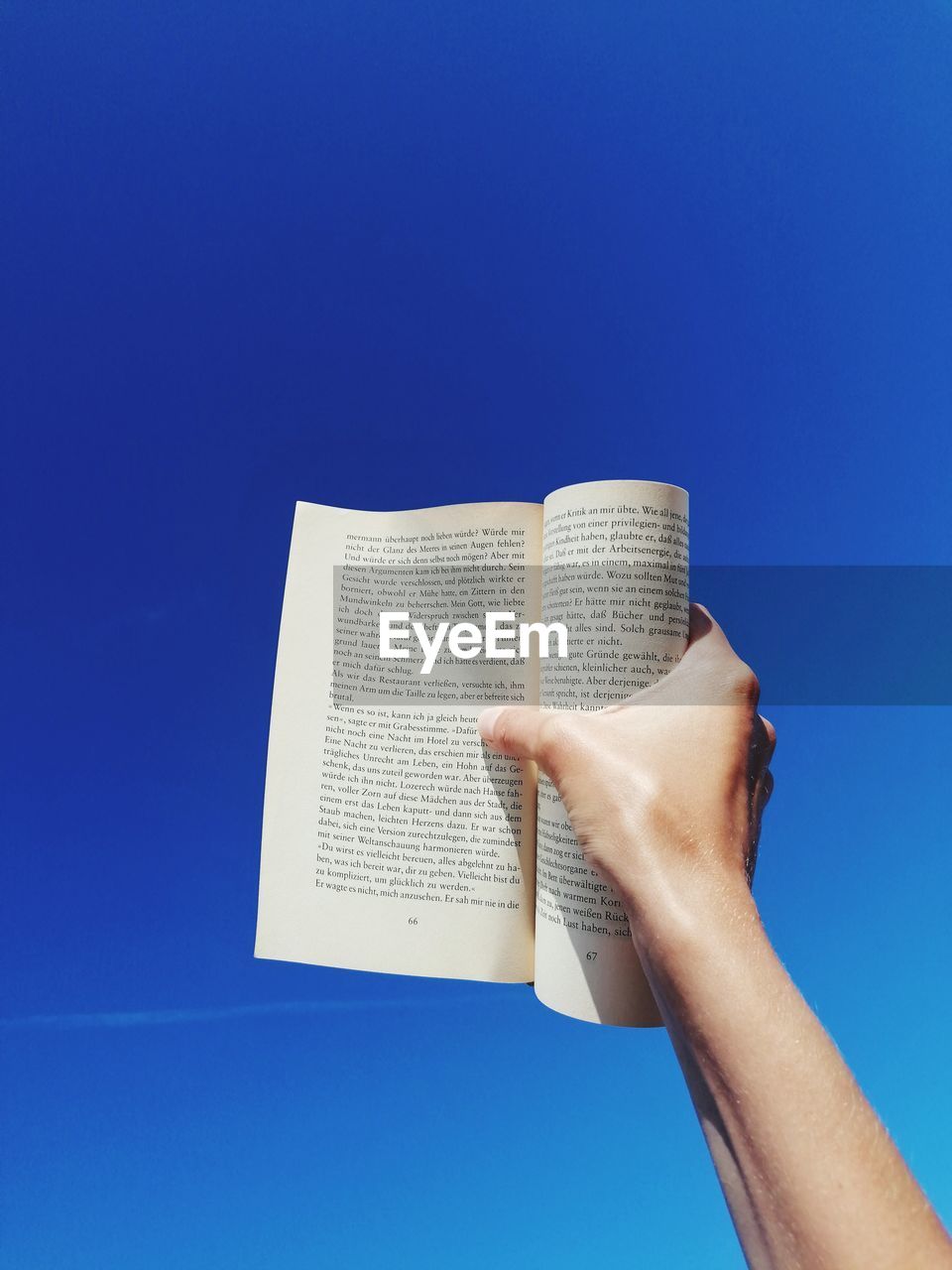 Cropped hand of person holding paper against blue background