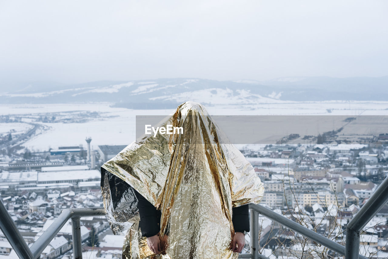 Person covered in golden paper standing against cityscape