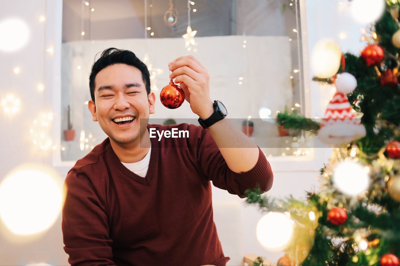 Portrait of woman holding christmas tree at home