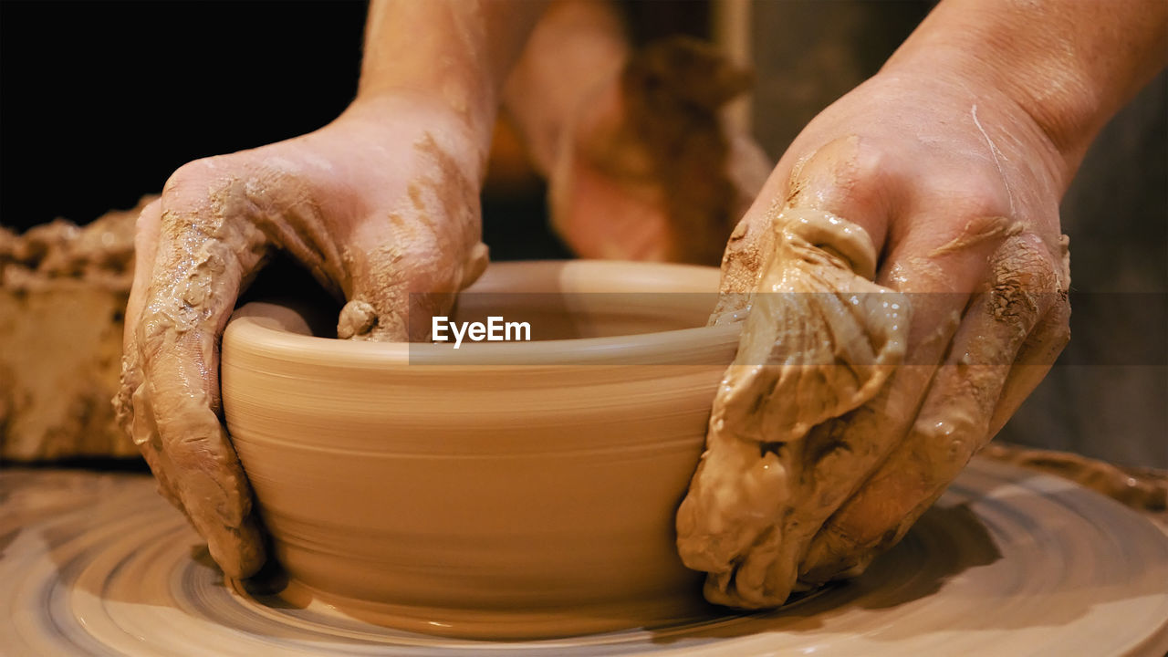 Cropped hands of craftsperson making clay product in pottery workshop