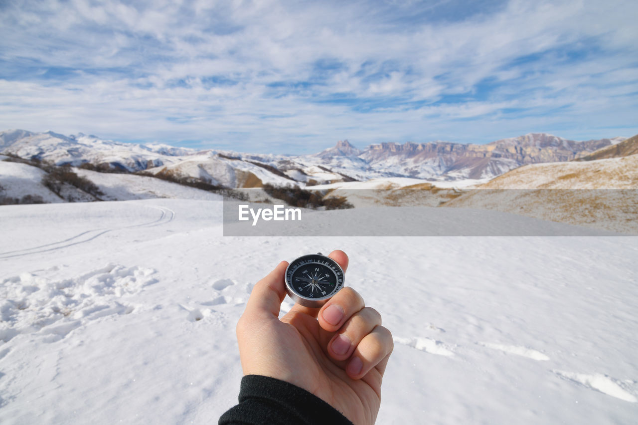 A man's hand holds a pocket magnetic compass for navigation against the backdrop of winter rocky 