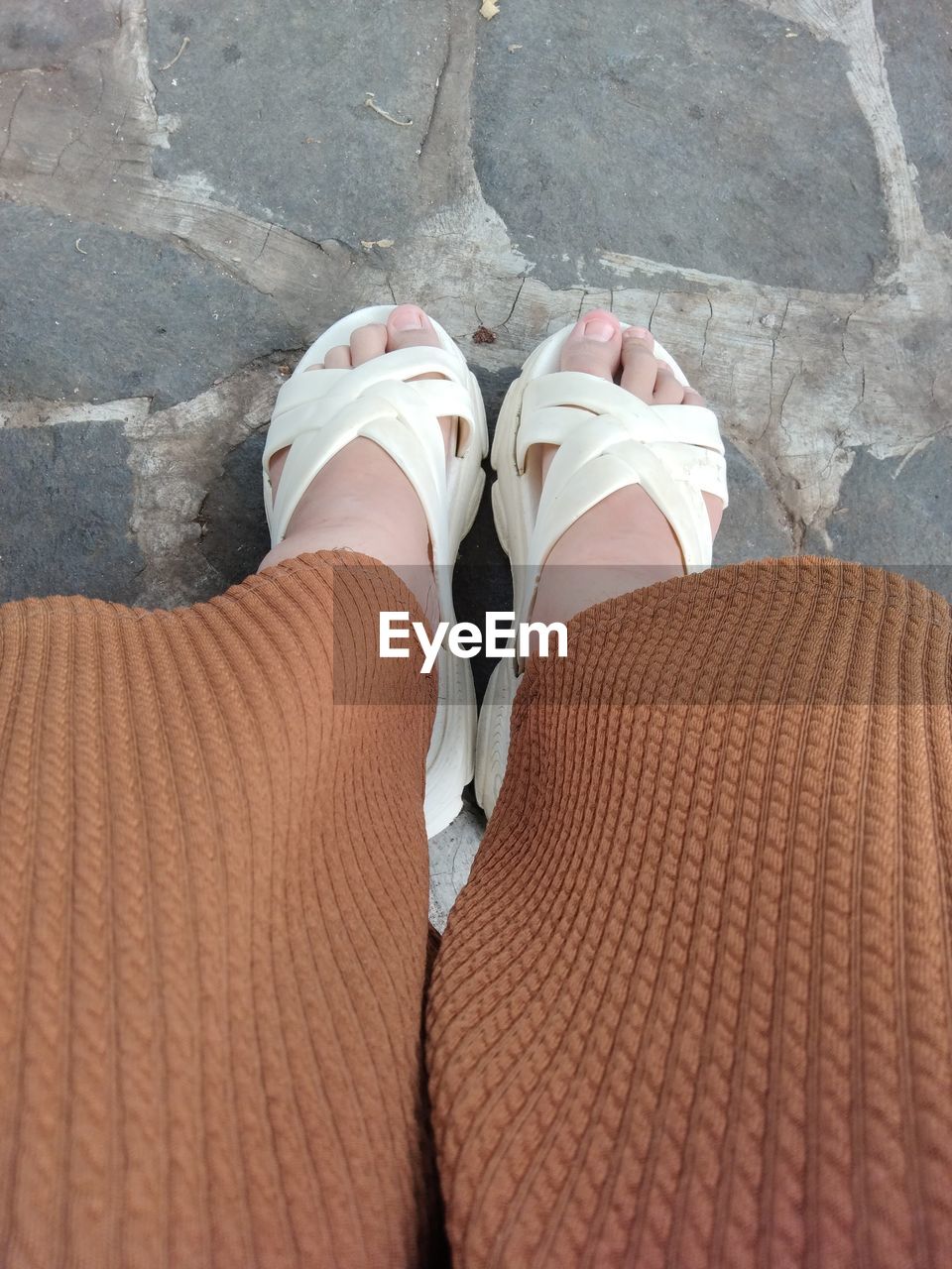 low section, human leg, shoe, footwear, one person, limb, personal perspective, high angle view, lifestyles, brown, standing, human limb, adult, day, women, sandal, leisure activity, clothing, hand, outdoors, human foot, footpath