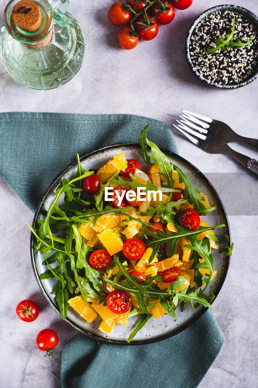 Dietary salad of orange slices, cherry tomatoes and arugula on a plate top and vertical view