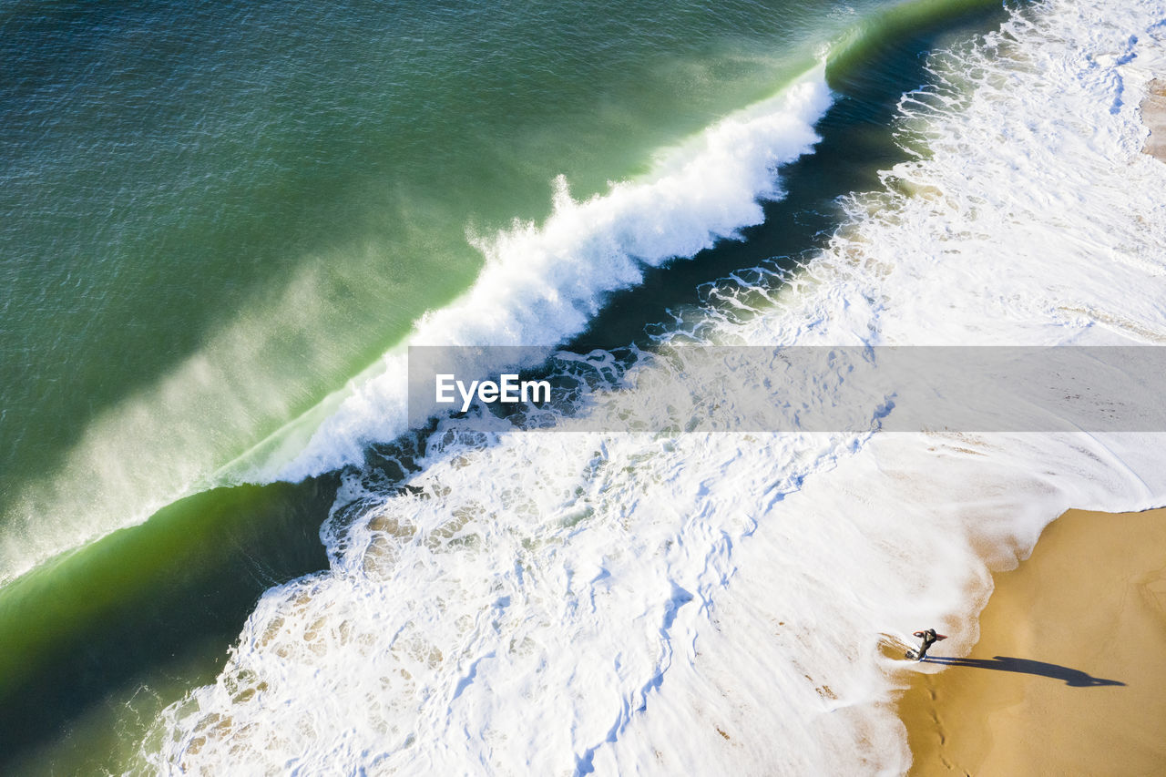 Bodyboard surfer watching shorebreak wave crashing on the beach aerial