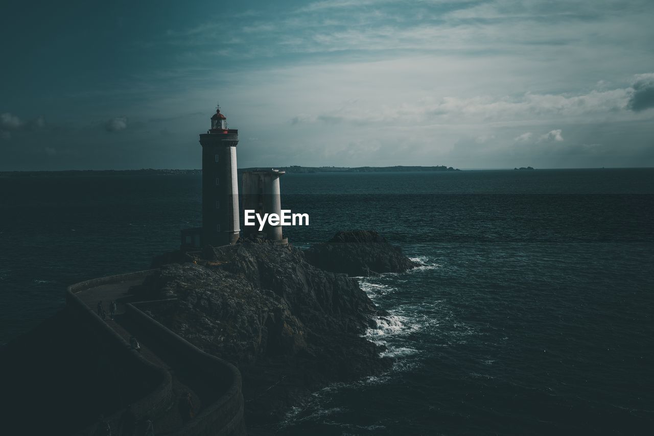 Lighthouse amidst sea and buildings against sky