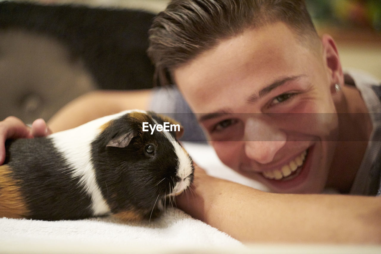 Close-up portrait of smiling man playing with guinea pig on bed at home