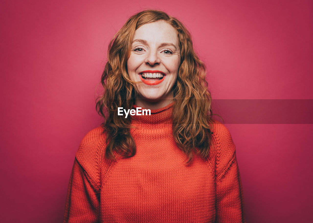 Portrait of smiling woman in orange top against pink background