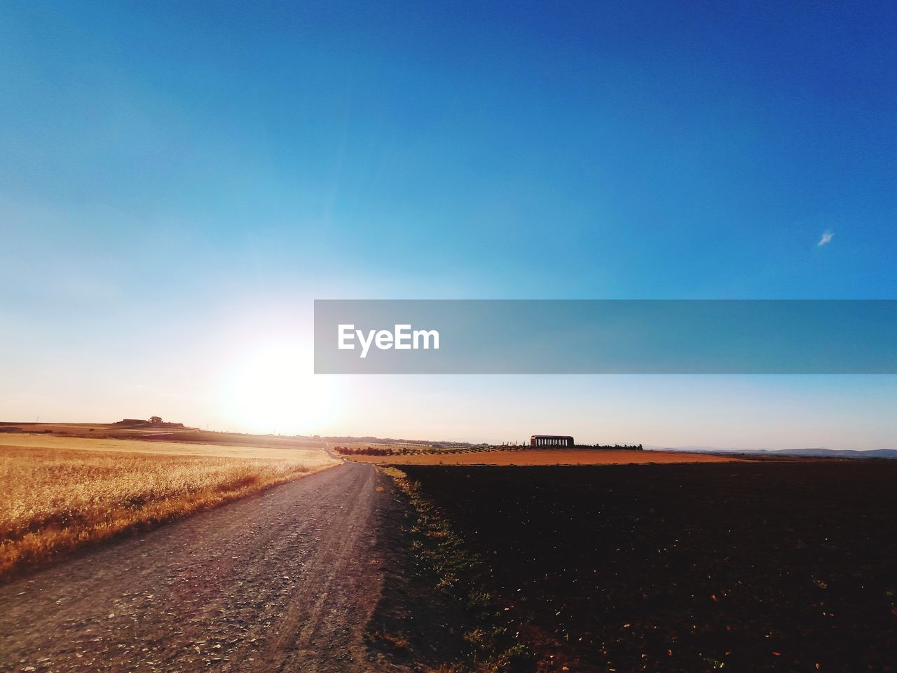 Road amidst field against sky during sunset