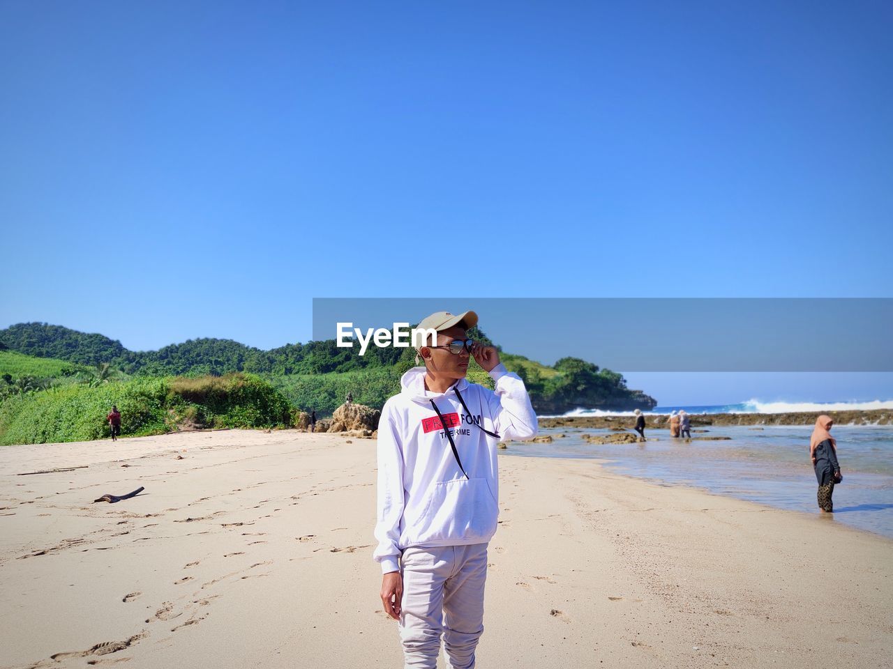 Rear view of man standing at beach against clear blue sky