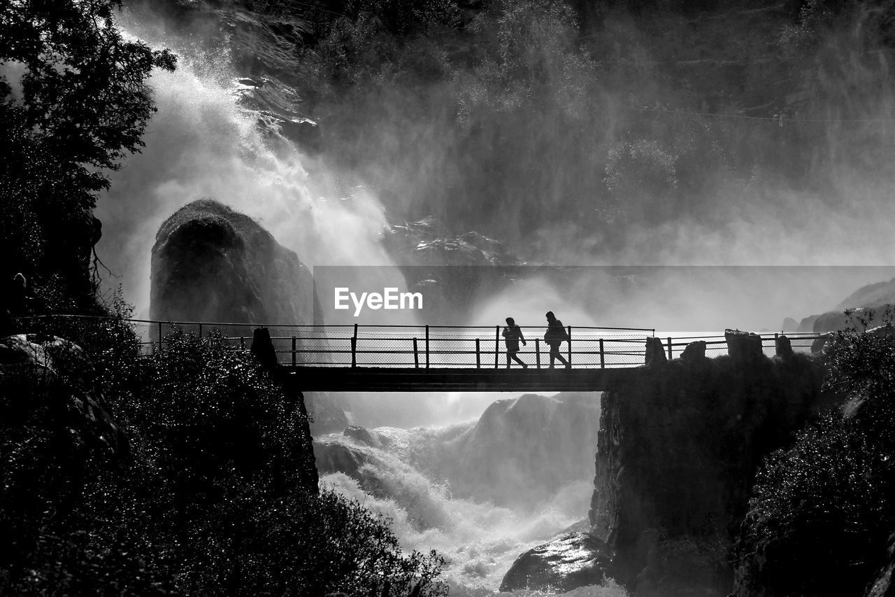 Silhouette people walking on bridge against waterfall