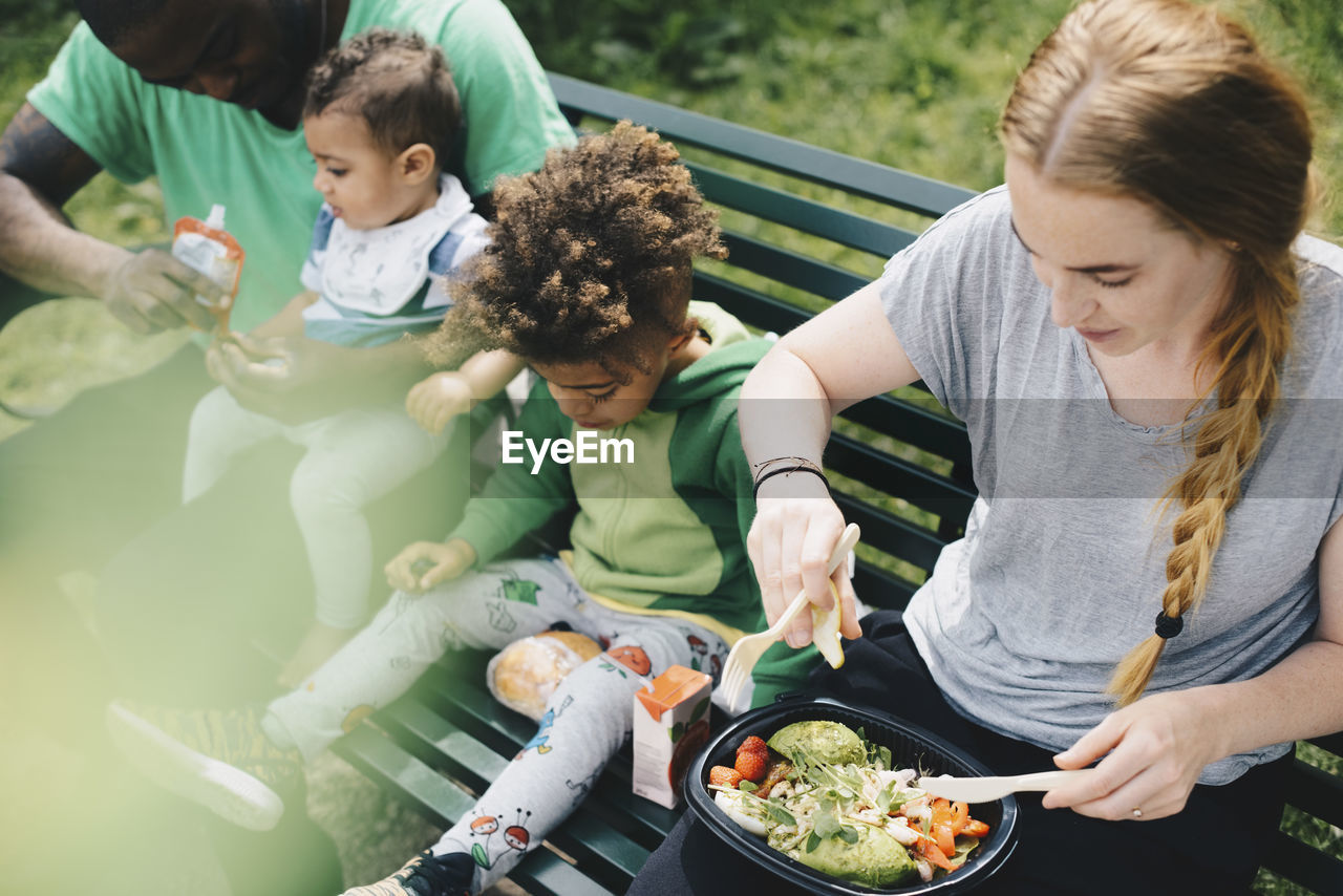 High angle view of family having food while sitting on bench at park