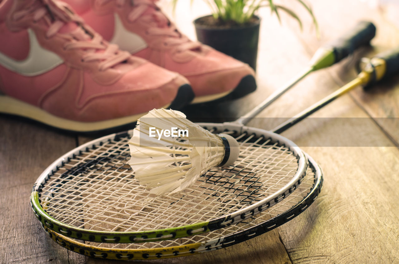 High angle view of rackets with shuttlecock and sports shoes on hardwood floor