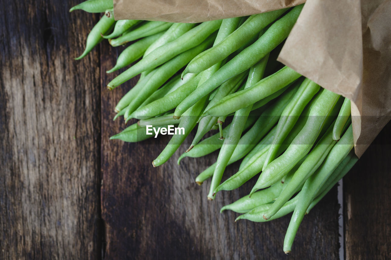 High angle view of green beans with wax paper on wooden table