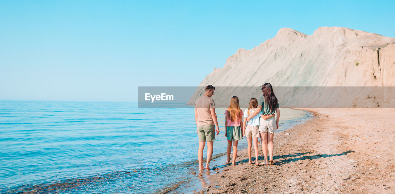 PEOPLE STANDING ON BEACH AGAINST SKY