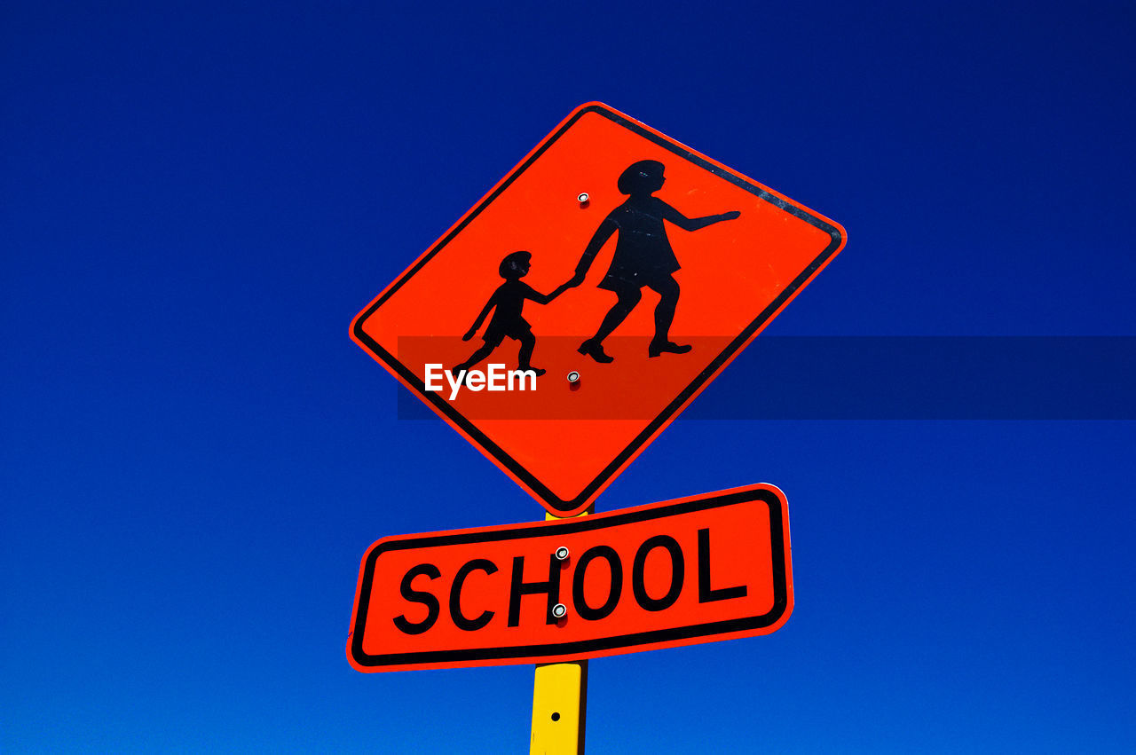 Low angle view of school crossing sign against clear blue sky