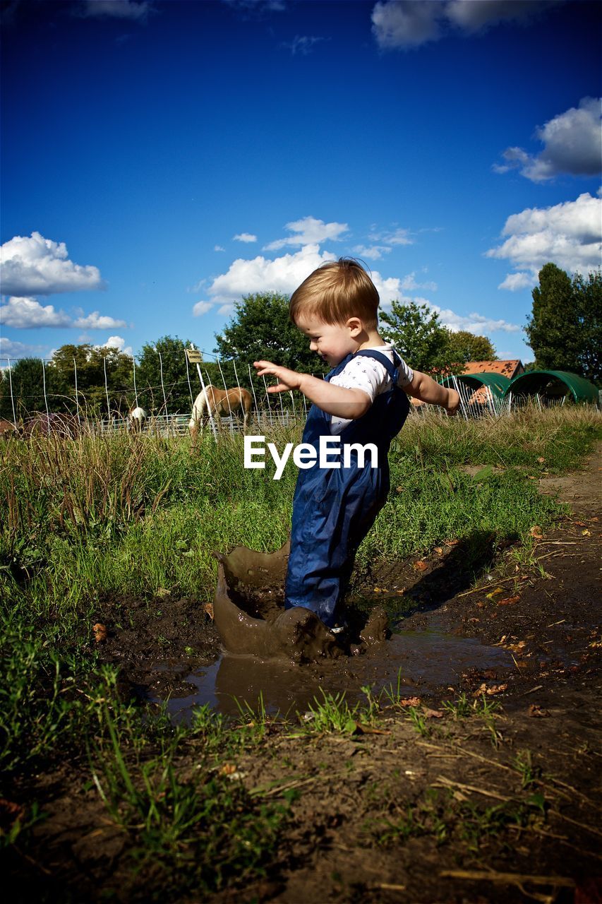 Full length of boy splashing mud on field against sky