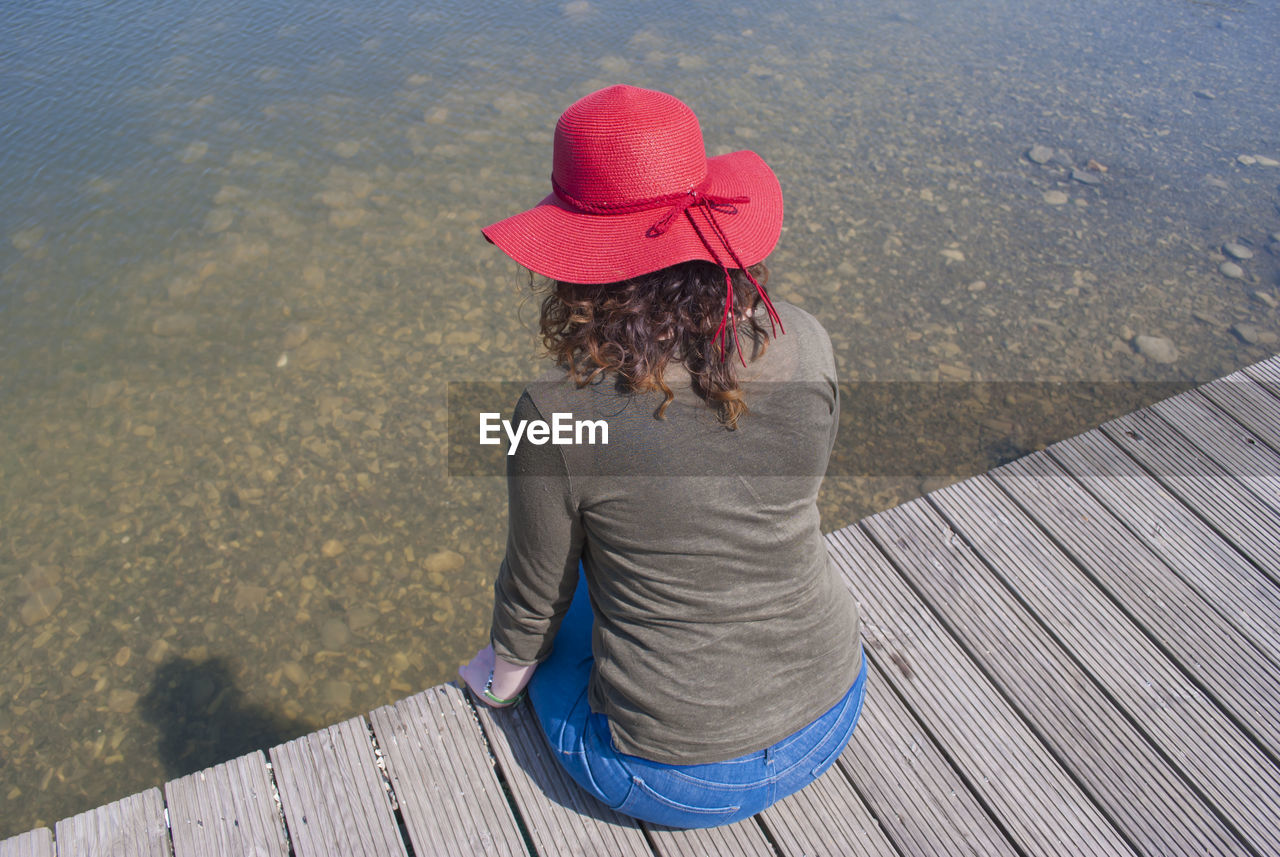 Woman in red hat sitting against lake