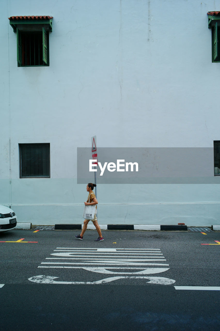 REAR VIEW OF WOMAN WALKING ON STREET AGAINST BUILDINGS