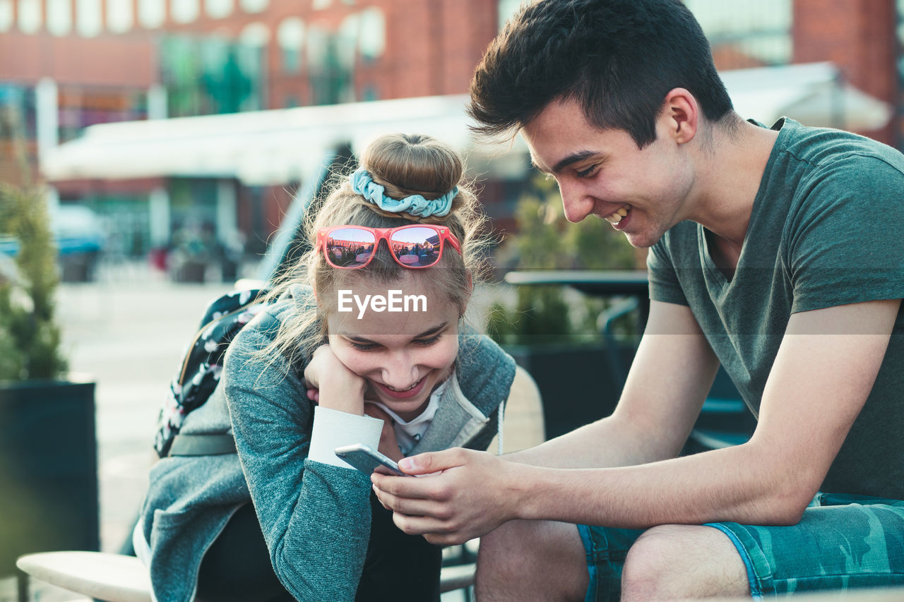 Smiling teenage friends using mobile phone in city