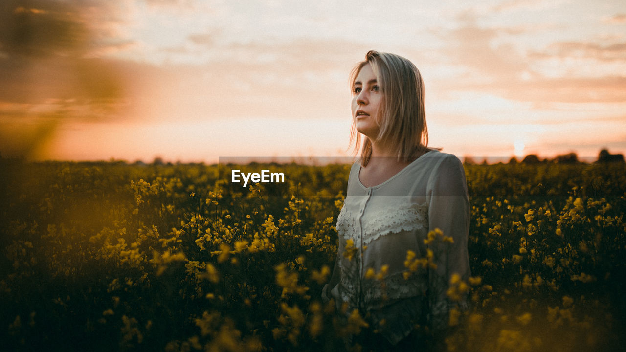 BEAUTIFUL WOMAN STANDING ON FIELD AGAINST YELLOW SKY