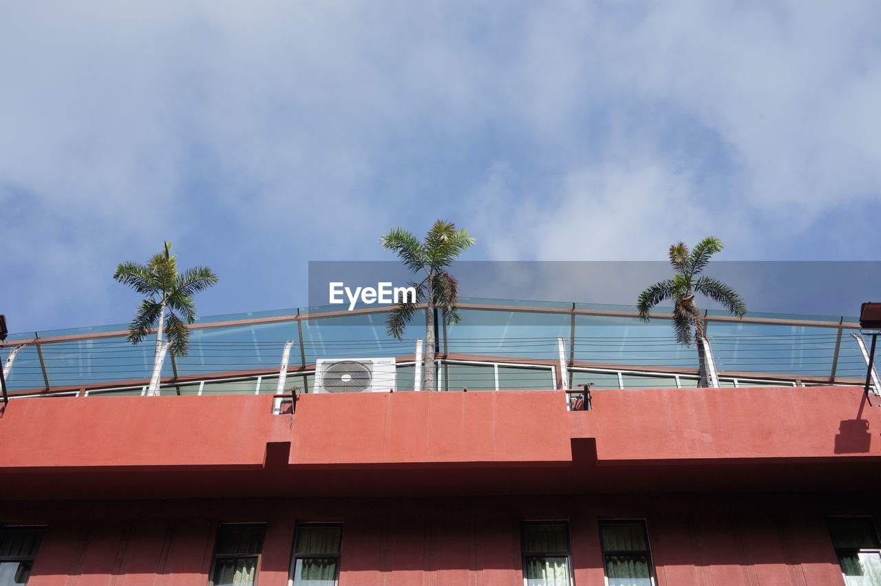 Low angle view of palm trees on building patio against cloudy sky