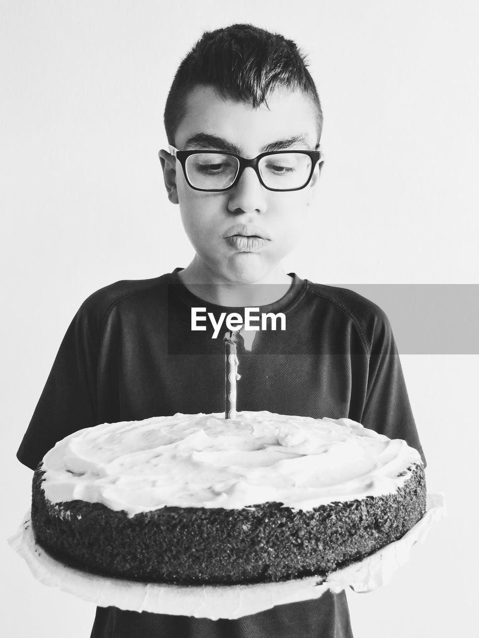 Boy blowing lit candle on cake against white background