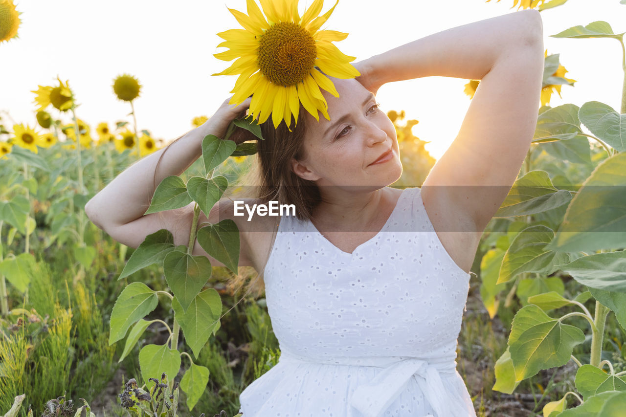 Smiling woman with arms raised holding sunflower on head