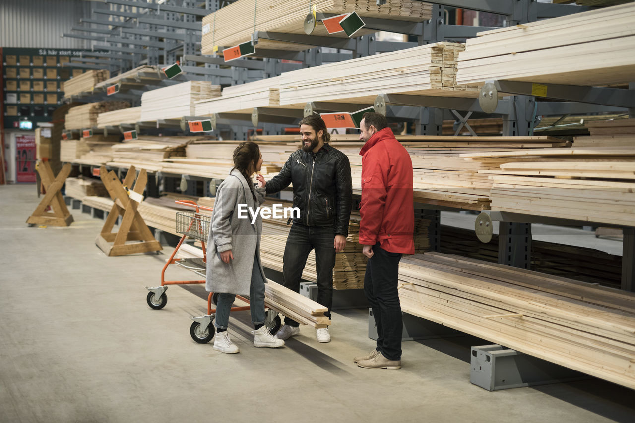 Customers and salesman standing by wooden planks on shelves in hardware store warehouse