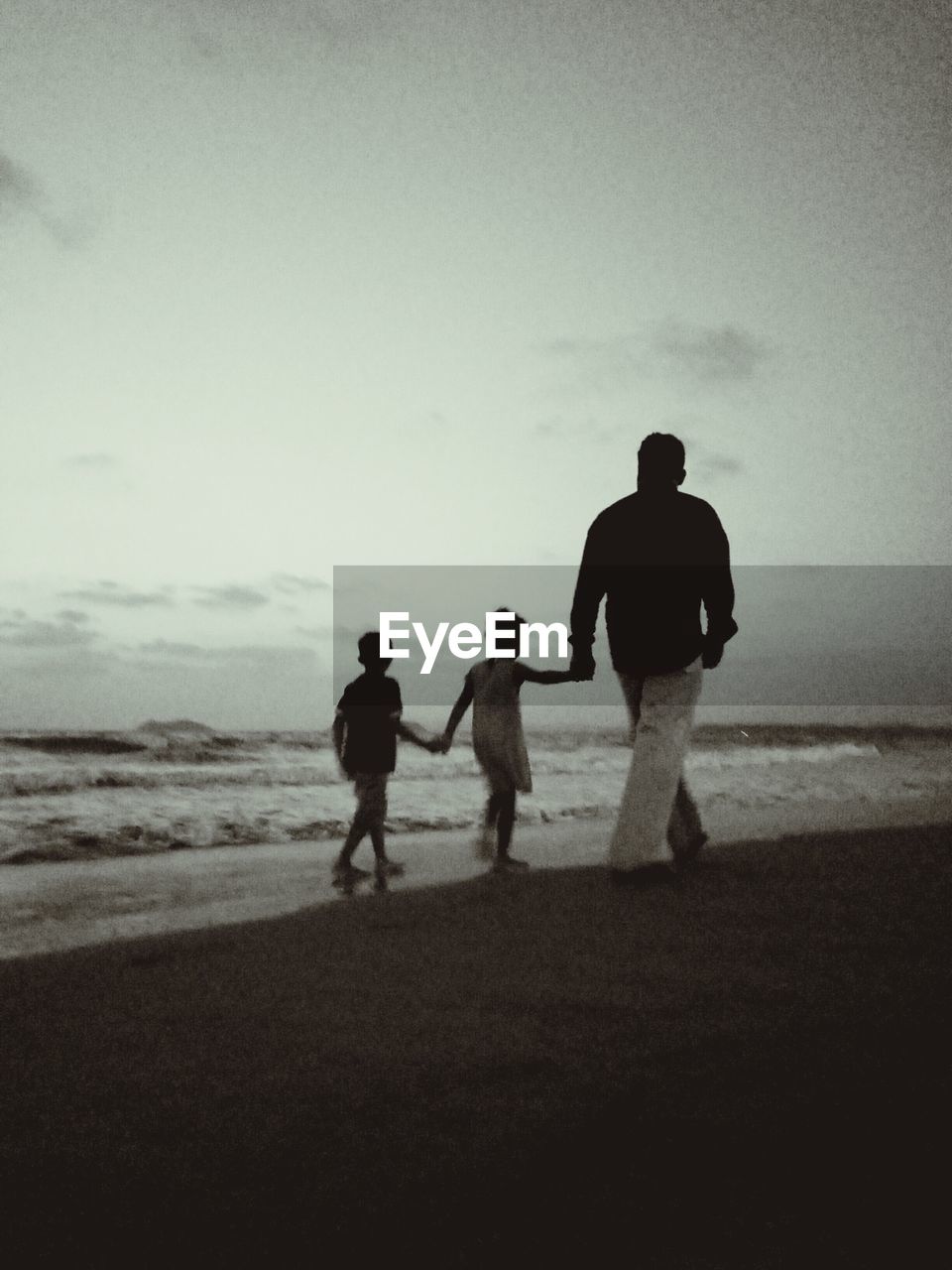 Rear view of family walking on shore at beach against sky