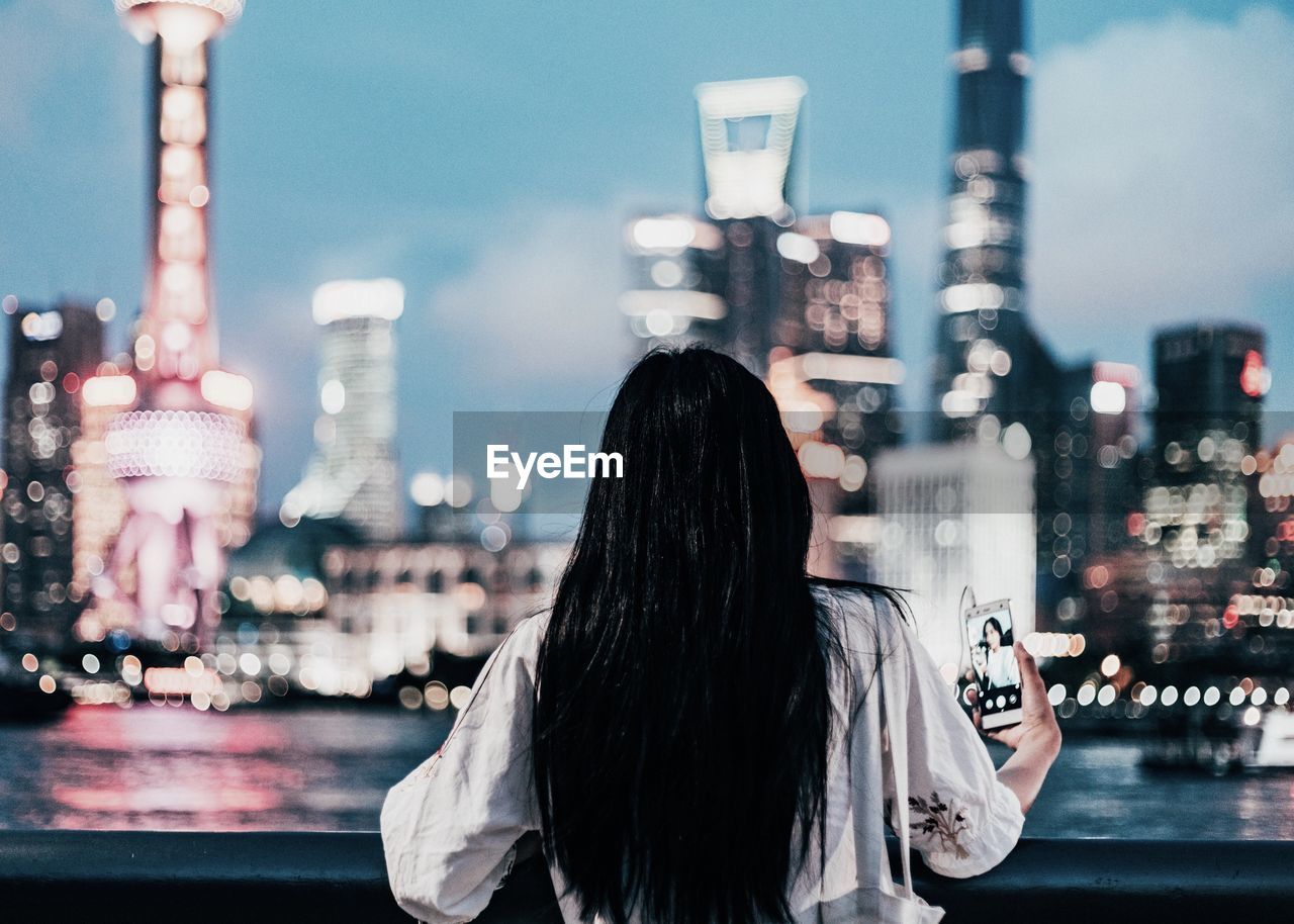 Rear view of girl against illuminated city at night