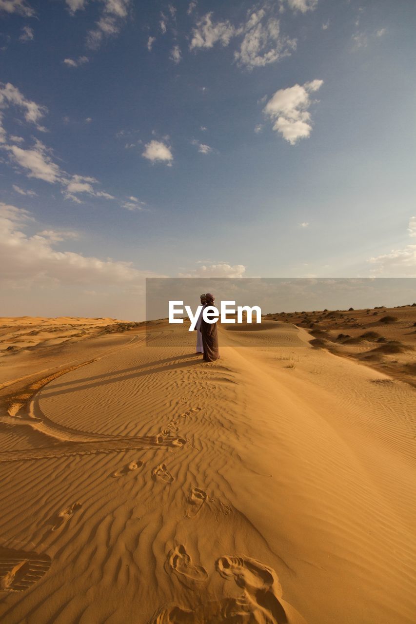 Men standing in arid landscape against sky on sunny day