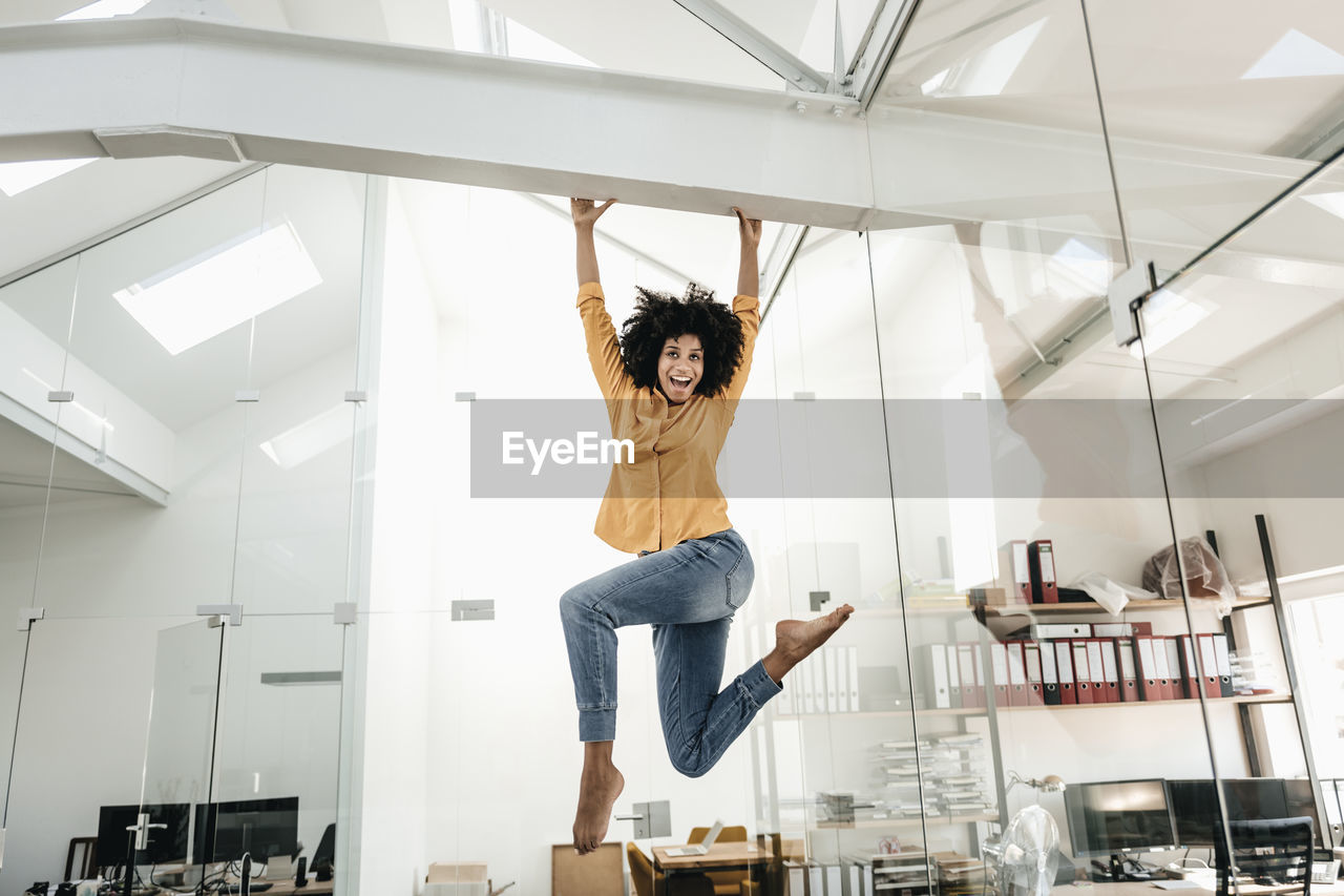 Happy young woman hanging on beam in office