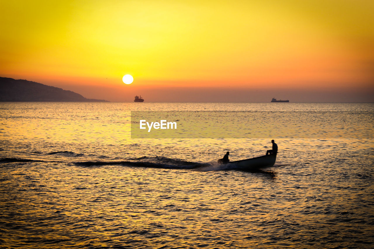 Scenic view of sea with people in boat against sky during sunset