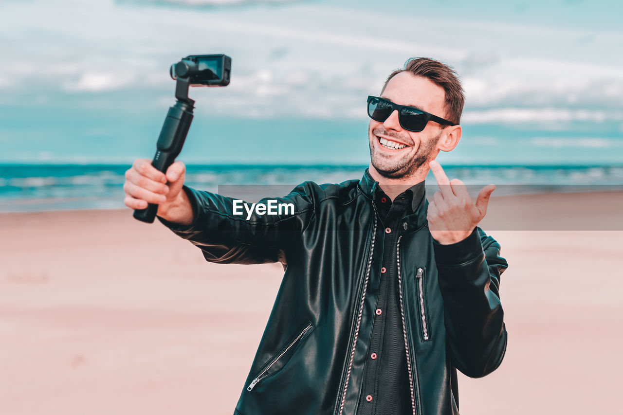 Smiling man gesturing while vlogging at beach