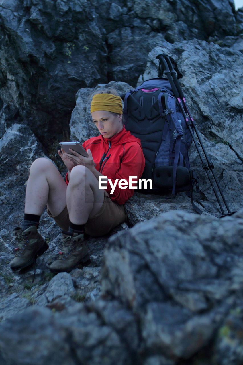 Full length of woman using digital tablet while sitting on rock formation