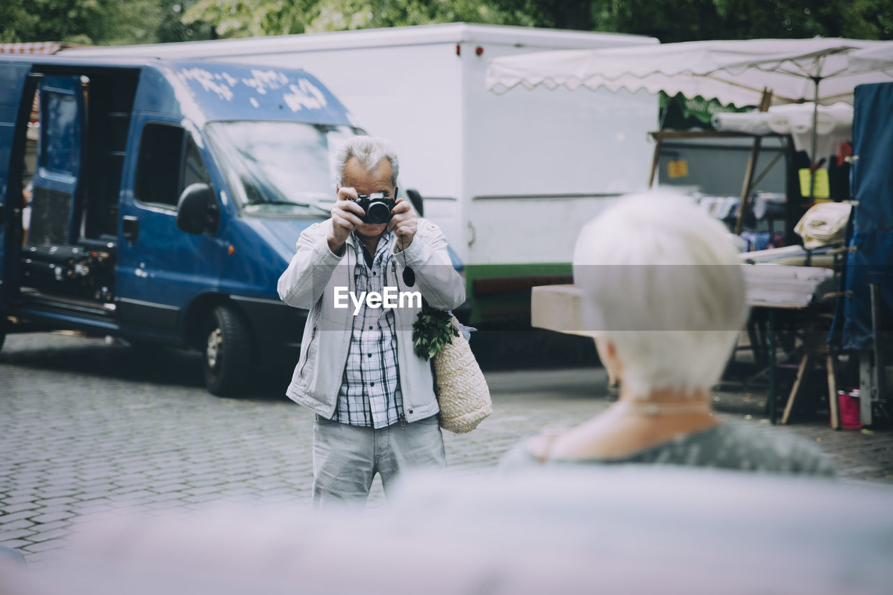 Senior tourist taking photograph of woman while standing in city