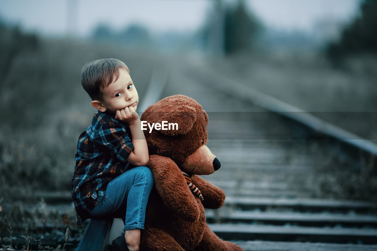 Boy with teddy bear sitting on railroad track