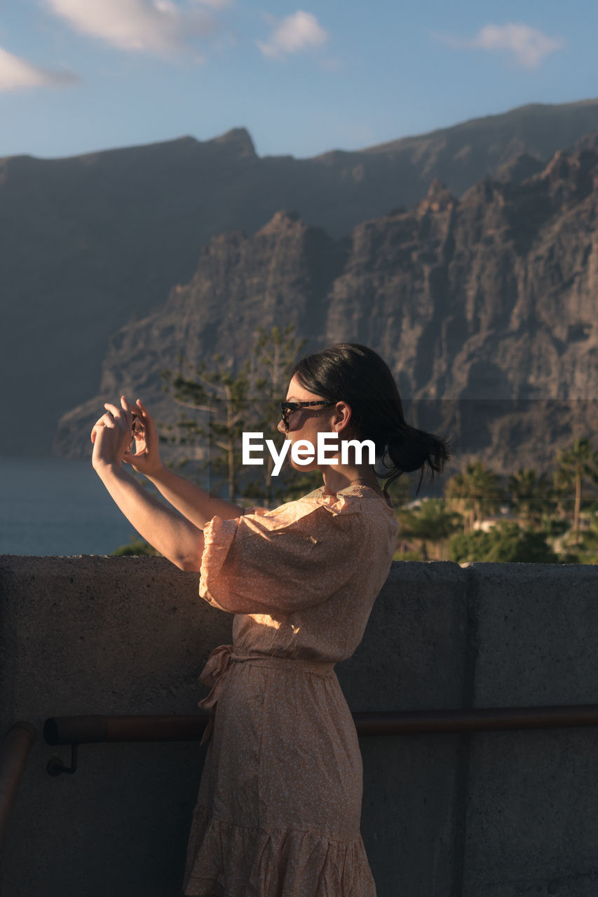 Woman looking at camera while standing on mountain against sky