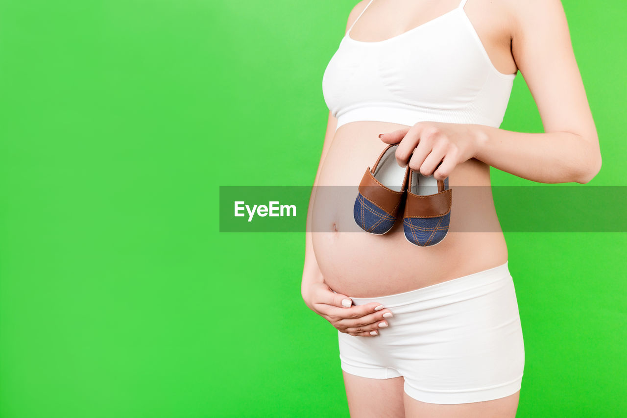 MIDSECTION OF WOMAN STANDING AGAINST GREEN WALL